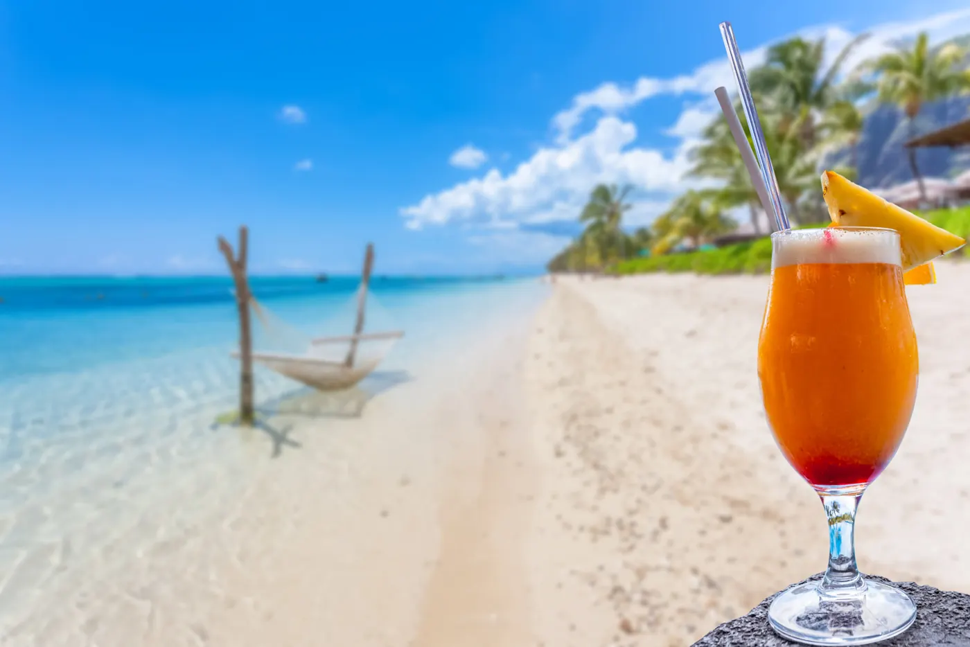 Painkiller cocktail with a pineapple garnish on a turquoise beach in bright daylight